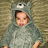 baby, child, face, tongue_out, costume, bear_costume, hood, soft_texture, blanket, cute, playful, smiling, lying_down, indoor, person, infant, cozy, warm_clothing, head, expression