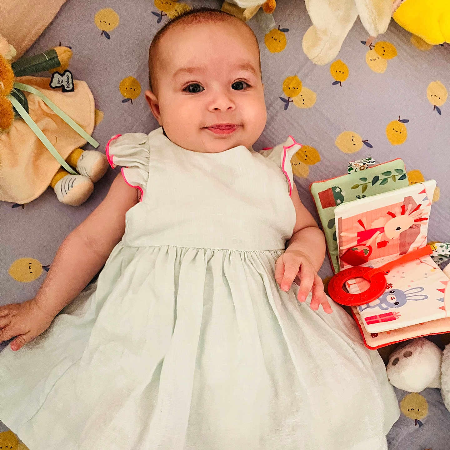 Juliette a rejoint le concours — aidez-le/la à gagner de superbes lots ! baby, blanket, book, child, colorful, cute, dress, face, hand, happy, indoors, infant, lying_down, patterned_blanket, person, playful, smiling, soft_toy, toy, young_child