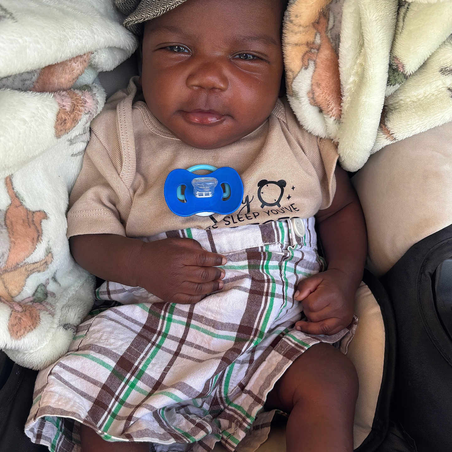 Knowledge is registered to the contest to win money with this photo: baby, infant, child, blanket, hat, pacifier, plaid, clothing, sitting, cute, portrait, closeup, smile, face, hand, footwear, cozy, indoor, soft, toddler