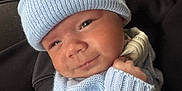 Reggie joined the competition — help win amazing prizes! baby, baby_clothes, blue_hat, couch, cozy, cute, face, hand, headwear, indoor, infant, knitwear, newborn, person, pom_pom, portrait, sitting, smile, tattoo, warm_clothing