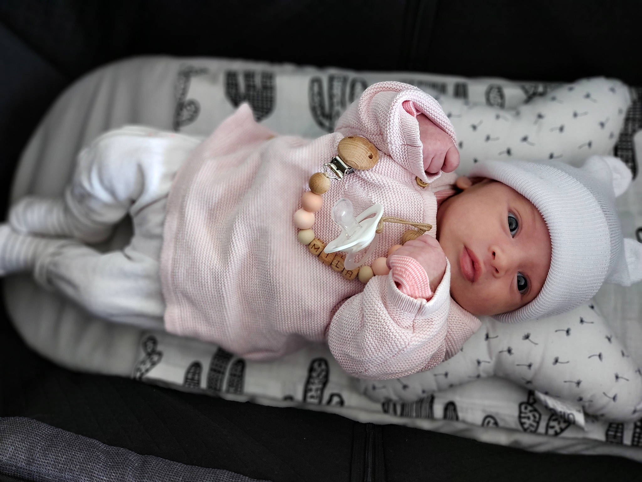 Mila participe au concours pour gagner de l'argent avec cette photo : arm, baby, baby_products, baby_toddler_clothing, cheek, child, comfort, dress, eye, hand, hat, headwear, linens, pattern, person, portrait_photography, room, sitting, skin, sleeve