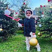 Jaya a rejoint le concours — aidez-le/la à gagner de superbes lots ! child, toddler, outdoor, christmas_tree, ornament, holiday, winter_clothing, grass, festive, toy, smiling, coat, hood, mittens, pants, shoes, nature, daylight, celebration, cute