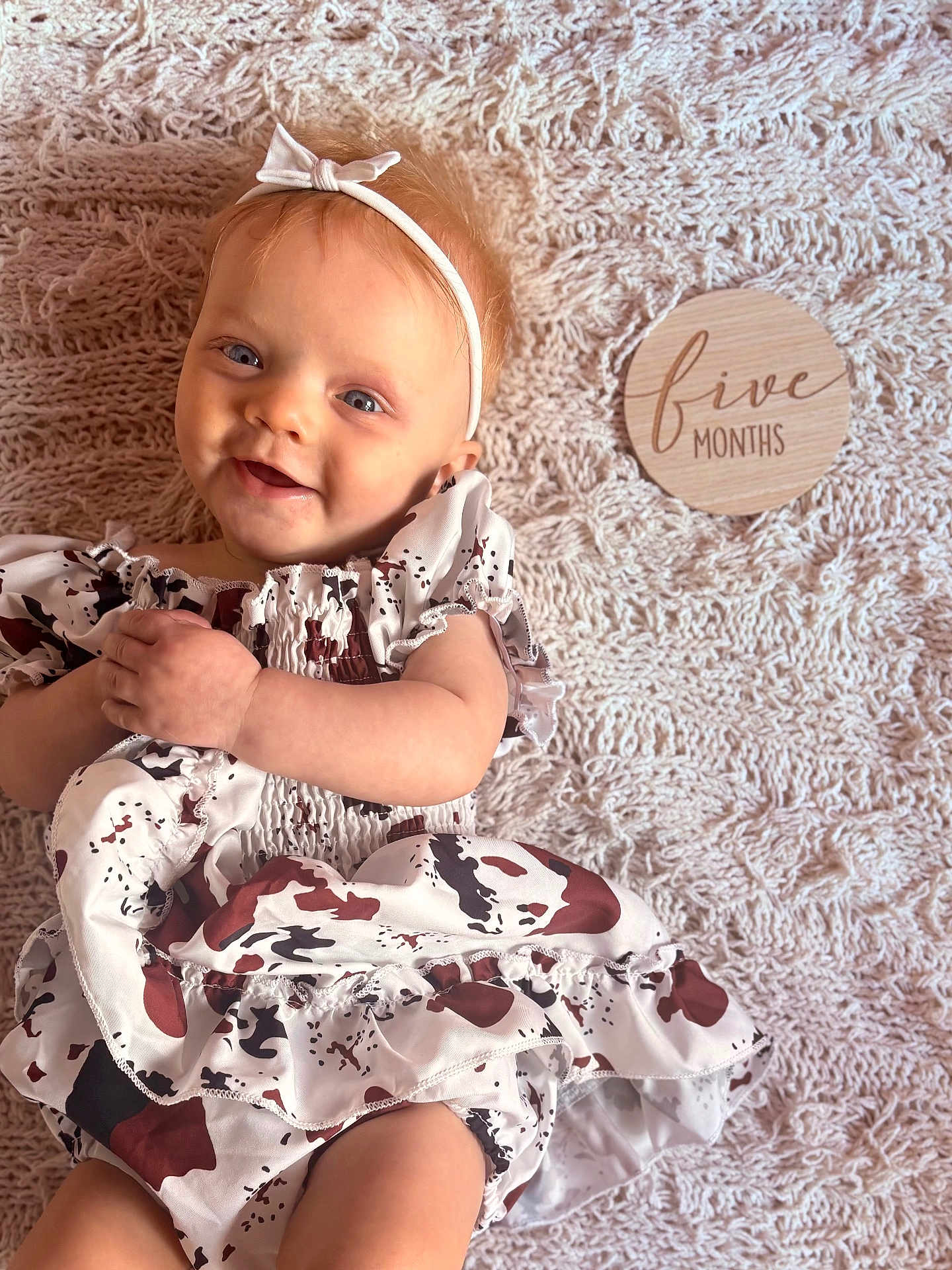 Elena is registered to the contest to win money with this photo: baby, infant, smiling, headband, bow, dress, patterned_clothing, blanket, knitted_blanket, wooden_sign, five_months, happy, cute, child, portrait, indoor, soft_lighting, skin, face, hands
