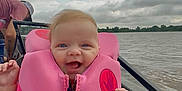 Elena joined the competition — help win amazing prizes! baby, life_jacket, water, boat, sky, clouds, hand, person, outdoor, smile, child, happy, transport, nature, people, watercraft, safety, pink, adult, daytime