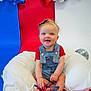 Elena joined the competition — help win amazing prizes! baby, child, smiling, denim_overalls, headband, glasses, star_shaped, pillow, red_background, blue_background, white_background, patriotic, indoor, sitting, cute, happy, portrait, infant, toy, face