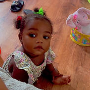 Ariah is registered to the contest to win money with this photo: toddler, child, floor, wooden_floor, toy, plush_elephant, basket, hair_bows, curious, indoor, slippers, cables, clothing, sitting, baby, expression, cute, home, person, playtime
