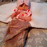 Naomi is registered to the contest to win money with this photo: baby, infant, pink_hat, bow, blanket, bear_pattern, cushion, elephant_pattern, laundry_basket, clothing, cute, soft_texture, lying_down, indoors, face, newborn, wrapped, cozy, looking, person