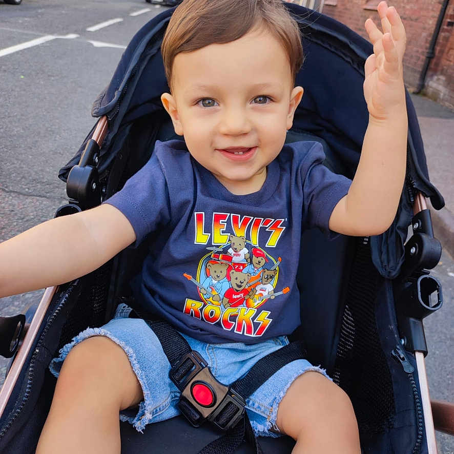 Enoh Ioan Sava is registered to the contest to win money with this photo: car, casual_clothing, child, cute, daylight, happy, outdoor, person, playful, safety_belt, shorts, sidewalk, smiling, street, stroller, toddler, tshirt, urban, waving, young_child