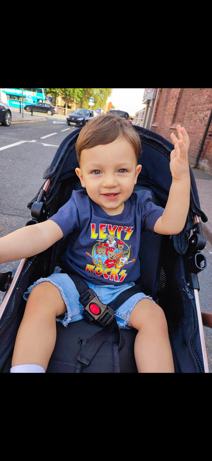 Enoh Ioan Sava is registered to the contest to win money with this photo: toddler, child, stroller, street, urban, casual_clothing, shorts, tshirt, smiling, waving, daylight, sidewalk, car, safety_belt, playful, outdoor, person, young_child, cute, happy