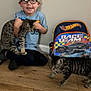 Luna And Leo joined the competition — help win amazing prizes! backpack, boy, casual_clothing, cat, child, floor, glasses, happy, home, hot_wheels, indoor, pets, playful, race_team, sitting, smiling, spotted_cat, striped_cat, wood_floor, young_child