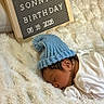 newborn, baby, sleeping, blue_hat, blanket, letter_board, birthday, soft_texture, white, wooden_frame, infant, cozy, cute, resting, indoor, person, headwear, announcement, celebration, closeup