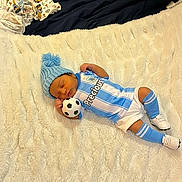 Sonny is registered to the contest to win money with this photo: baby, infant, soccer_ball, blue_hat, knit_hat, blanket, sports_uniform, socks, shoes, sleeping, indoor, soft_texture, baby_clothes, toy, resting, cute, child, lying_down, home, sleep