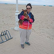 Snickers joined the competition — help win amazing prizes! beach, bike_rack, brown_dog, calm, casual_clothing, daytime, dog, footwear, glasses, holding, jacket, lamp_post, ocean, outdoor, overcast_sky, person, pet, sand, small_dog, standing