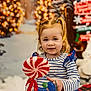 toddler, child, lollipop, candy, striped_shirt, pigtails, smile, winter, snow, snowman, christmas_tree, holiday, festive, decorations, indoor, portrait, cute, happy, toy, background