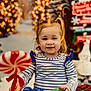 toddler, child, smiling, pigtails, striped_shirt, candy, holiday, christmas, snowman, lights, festive, winter, decorations, background, indoor, toy, red, white, blue, happy