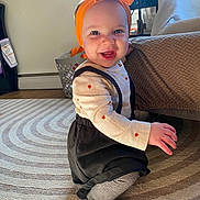 Marina joined the competition — help win amazing prizes! baby, child, smiling, headband, orange, bow, long_sleeve_shirt, suspenders, striped_tights, socks, rug, carpet, indoor, furniture, laundry_basket, natural_light, happy, cute, person, floor