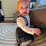 baby, child, smiling, headband, orange, bow, long_sleeve_shirt, suspenders, striped_tights, socks, rug, carpet, indoor, furniture, laundry_basket, natural_light, happy, cute, person, floor