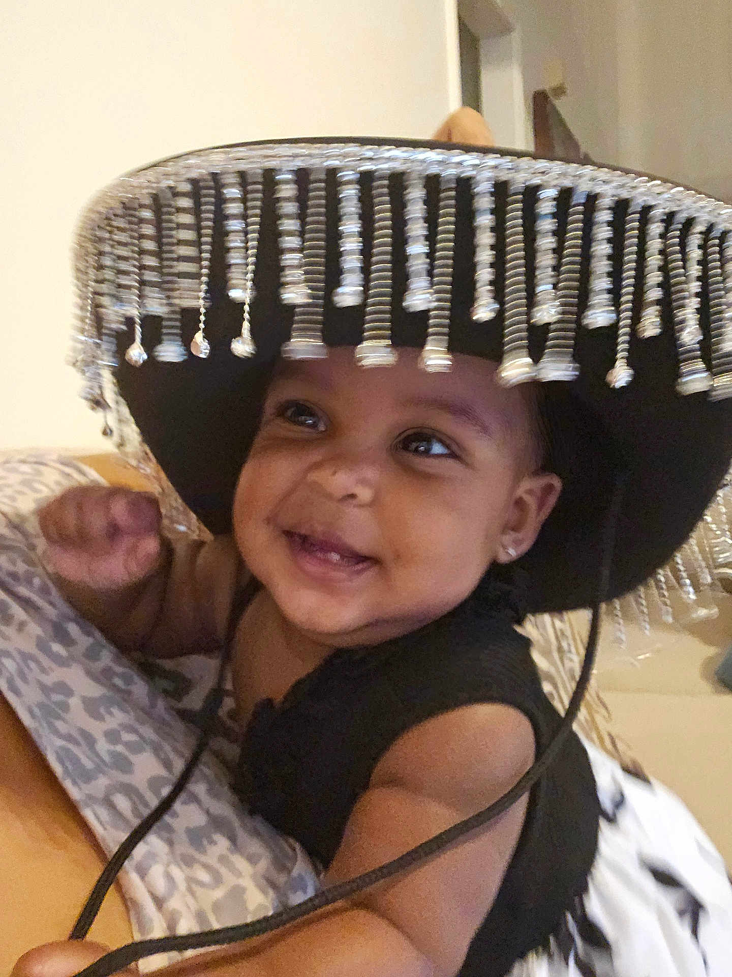 Layla is registered to the contest to win money with this photo: baby, smiling, hat, sombrero, beads, child, cute, indoors, blanket, pattern, face, portrait, happy, infant, clothing, person, young_child, skin, earrings, black_top