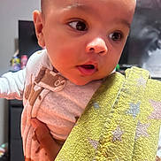 Jamaree is registered to the contest to win money with this photo: baby, child, face, blanket, hand, indoor, curious, wide_eyes, yellow, star_pattern, clothing, person, portrait, toddler, soft_lighting, warm_colors, holding, infant, close_up, expression
