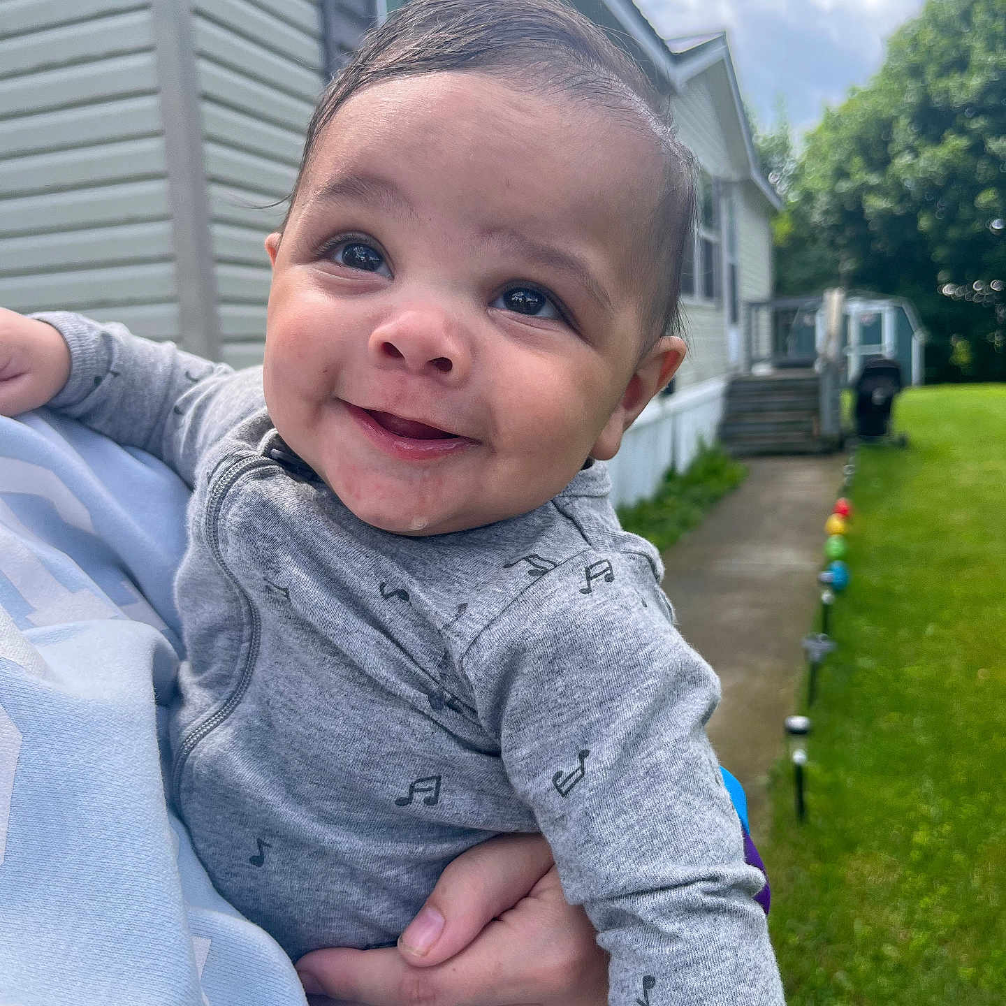 Jamaree is registered to the contest to win money with this photo: baby, child, smile, face, person, outdoor, house, clothing, hand, grass, sky, cloud, window, music_note_pattern, yard, holding, cute, portrait, happy, daylight