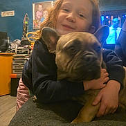 Stitch a rejoint le concours — aidez-le/la à gagner de superbes lots ! child, dog, french_bulldog, hugging, indoor, couch, blue_wall, furniture, portrait, smiling, curly_hair, cozy, home, person, pet, casual_clothing, table, room, yellow_cabinet, photography