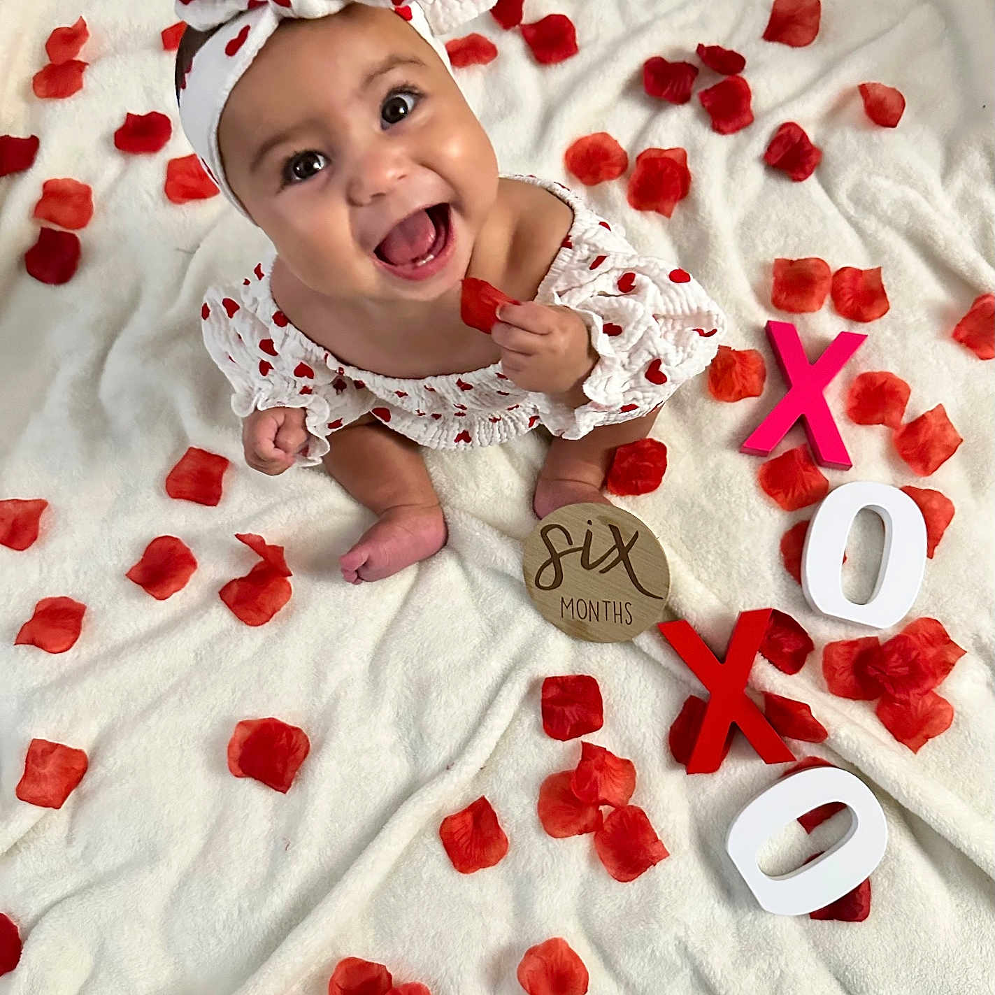 Gianna joined the competition — help win amazing prizes! baby, celebration, clothing, cute, decor, face, feet, hand, happy, headband, infant, portrait, red_hearts, rose_petals, sitting, six_months, smiling, white_blanket, wooden_letters, xoxo