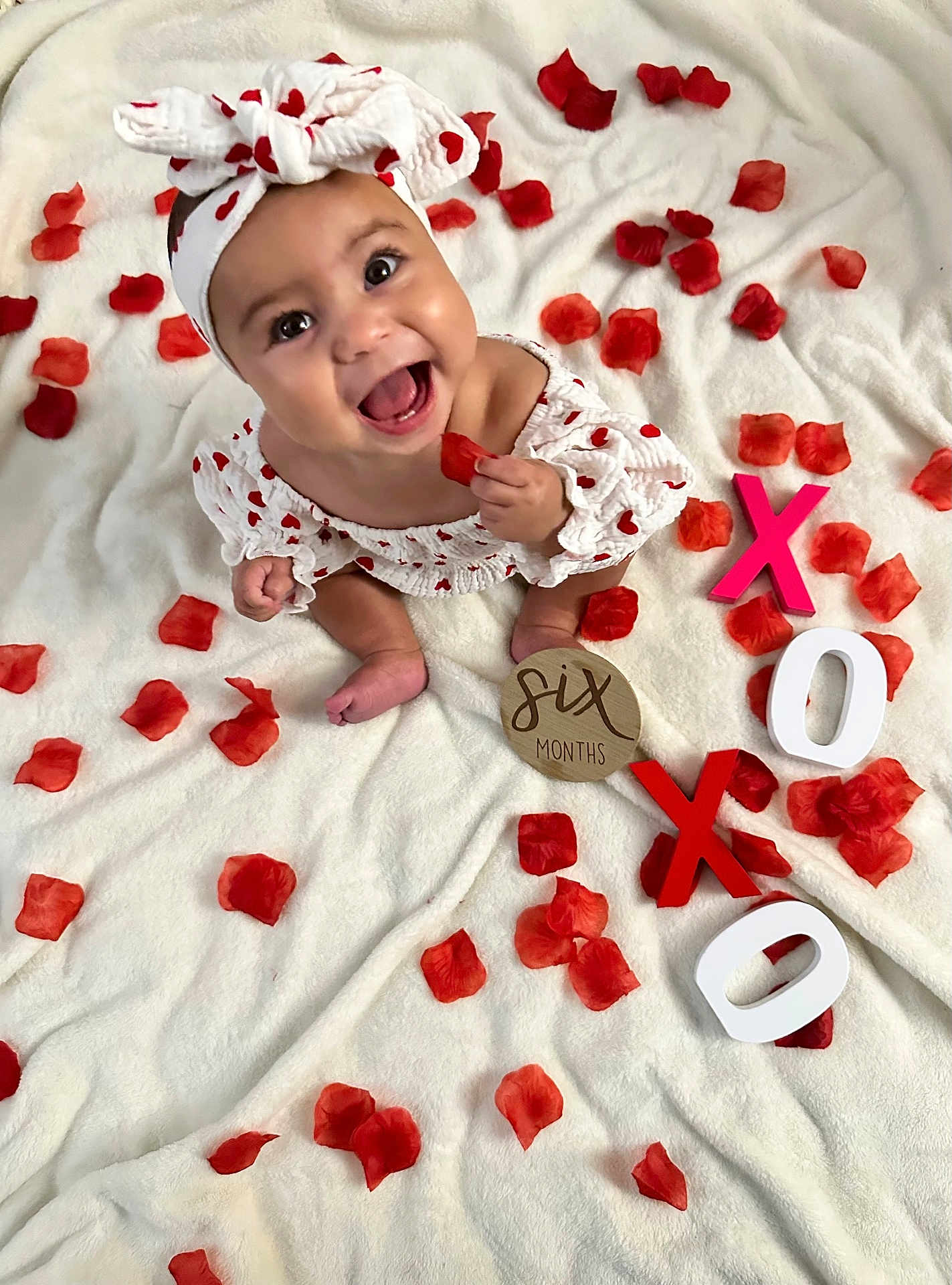 Gianna joined the competition — help win amazing prizes! baby, infant, headband, red_hearts, white_blanket, rose_petals, smiling, happy, six_months, wooden_letters, xoxo, cute, sitting, clothing, face, hand, feet, portrait, decor, celebration