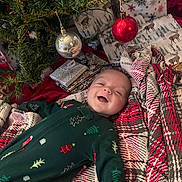 Hunter joined the competition — help win amazing prizes! baby, smiling, christmas_tree, ornament, red_ornament, silver_ornament, gift_wrap, holiday, festive_clothing, blanket, patterned_blanket, wrapped_presents, indoor, holiday_decor, cheerful, infant, lying_down, green_onesie, cozy, celebration