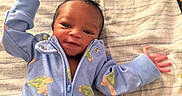 Mias Abram is registered to the contest to win money with this photo: baby, infant, smiling, blue_onesie, turtle_print, lying_down, hand_raised, blanket, bottle, bed, happy, cute, small_hands, newborn, child, person, portrait, cozy, indoor, soft_lighting