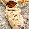 newborn, baby, swaddle, hat, sleeping, blanket, dinosaur_pattern, cozy, infant, soft_texture, cute, resting, child, indoor, portrait, wrapped, peaceful, warm, nursery, sleep