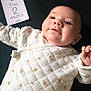 baby, infant, face, clothing, quilted, pattern, white, leaf, milestone_card, text, black_background, closeup, cute, lying_down, portrait, cheeks, hand, skin, expression, indoors