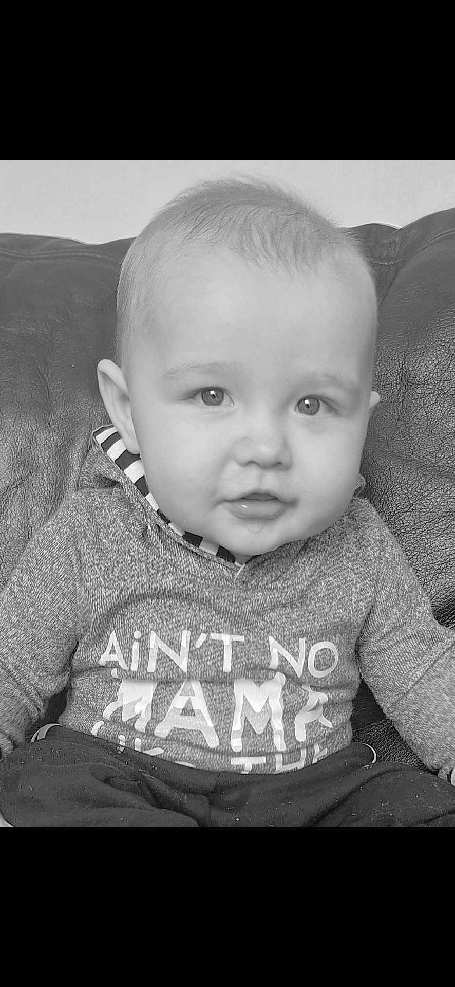 Callum is registered to the contest to win money with this photo: baby, infant, child, portrait, black_and_white, sweater, clothing, couch, leather, face, eyes, hair, mouth, sitting, cute, indoors, expression, person, young, cozy