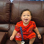 Jared Elías is registered to the contest to win money with this photo: baby, child, toddler, smiling, happy, curly_hair, portrait, sitting, leather_couch, recliner, orange_outfit, racing_theme, number_95, sandals, pacifier, blue_curtains, indoor, home, fashion, photography
