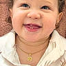 baby, child, toddler, portrait, smiling, tongue_out, curly_hair, blue_eyes, sitting, indoors, close_up, face, necklace, pendant, shirt, patterned_clothing, floral_pattern, brown_background, happy, photography