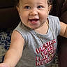 toddler, child, baby, smiling, happy, portrait, curly_hair, blue_eyes, indoor, leather_chair, seated, gray_shirt, necklace, outstretched_hand, carpet, home, close_up, photograph, casual_clothing, joyful
