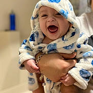 Aiden is registered to the contest to win money with this photo: baby, child, smiling, happy, hooded_robe, blue, white, polka_dots, hand, bracelet, indoor, person, portrait, cute, infant, laughing, clothing, warm, soft, holding