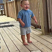 Aiden joined the competition — help win amazing prizes! toddler, child, barefoot, blue_tshirt, gray_shorts, wooden_deck, railing, outdoor, smiling, happy, standing, wood, person, casual_clothing, daylight, young_child, expression, portrait, natural_light, fun