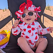 Jade is registered to the contest to win money with this photo: baby, child, sunglasses, hat, strawberry_pattern, swimwear, beach_chair, beach, sand, inflatable_toy, smile, happy, sunny, outdoor, summer, toddler, feet, clothing, seat, relaxation