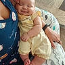 baby, sleeping, infant, yellow_outfit, adult, navy_shirt, dog_prints, cushion, whale_pattern, hand, arm, skin, comfort, rest, indoor, soft_lighting, closeup, peaceful, cute, smile