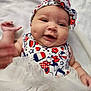 Kalista is registered to the contest to win money with this photo: baby, smile, headband, dress, dimples, lying, blanket, cute, infant, happy, clothing, colorful, pattern, cartoon, red, white, blue, face, child, portrait