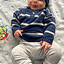 Cohen is registered to the contest to win money with this photo: baby, child, infant, blue_hat, striped_sweater, white_pants, sneakers, toy_ball, blanket, playful, tongue_out, cute, smiling, lying_down, soft_texture, indoor, portrait, cozy_clothing, headwear, hand
