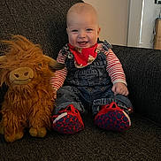 Cohen is registered to the contest to win money with this photo: baby, infant, smile, denim_overalls, striped_shirt, red_bandana, red_shoes, stuffed_animal, plush_toy, yak_toy, couch, indoor, happy, child, person, seated, cozy, home, furniture, cute