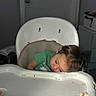 Kali is registered to the contest to win money with this photo: toddler, child, sleeping, high_chair, green_shirt, food_crumbs, indoor, tray, face, head, furniture, door, person, resting, casual, young_child, home, dim_light, hair, seat