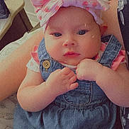 Mallory is registered to the contest to win money with this photo: baby, infant, child, denim_overalls, pink_bow, headwear, face, hands, indoor, person, furniture, couch, blanket, portrait, cute, young_child, skin, clothing, sitting, holding