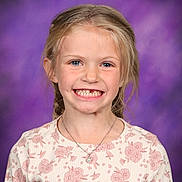 Quinn is registered to the contest to win money with this photo: child, girl, smiling, portrait, braids, missing_tooth, necklace, floral_pattern, long_sleeves, blue_eyes, blonde_hair, studio_background, purple_background, happy, cute, school_photo, casual_clothing, young, female, face
