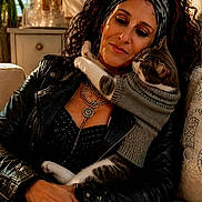 Liliane Libertini a rejoint le concours — aidez-le/la à gagner de superbes lots ! affection, cat, couch, cozy, cuddling, curly_hair, curtains, headband, home_decor, indoor, leather_jacket, necklace, pet, portrait, rings, sunlight, sweater, text_overlay, window, woman