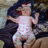 arms, baby, bed, blanket, bow, butterfly_pattern, child, colorful, face, headband, home, indoor, infant, legs, lying_down, pajamas, pink_clothing, portrait, smiling, text_on_clothing