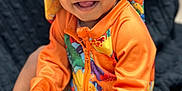 Kross is registered to the contest to win money with this photo: toddler, child, smiling, colorful_clothing, hat, orange_jacket, dinosaur_pattern, happy, sitting, indoors, portrait, baby, cute, hands, face, eyes, feet, blanket, texture, playful