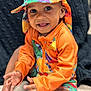 toddler, child, smiling, colorful_clothing, hat, orange_jacket, dinosaur_pattern, happy, sitting, indoors, portrait, baby, cute, hands, face, eyes, feet, blanket, texture, playful