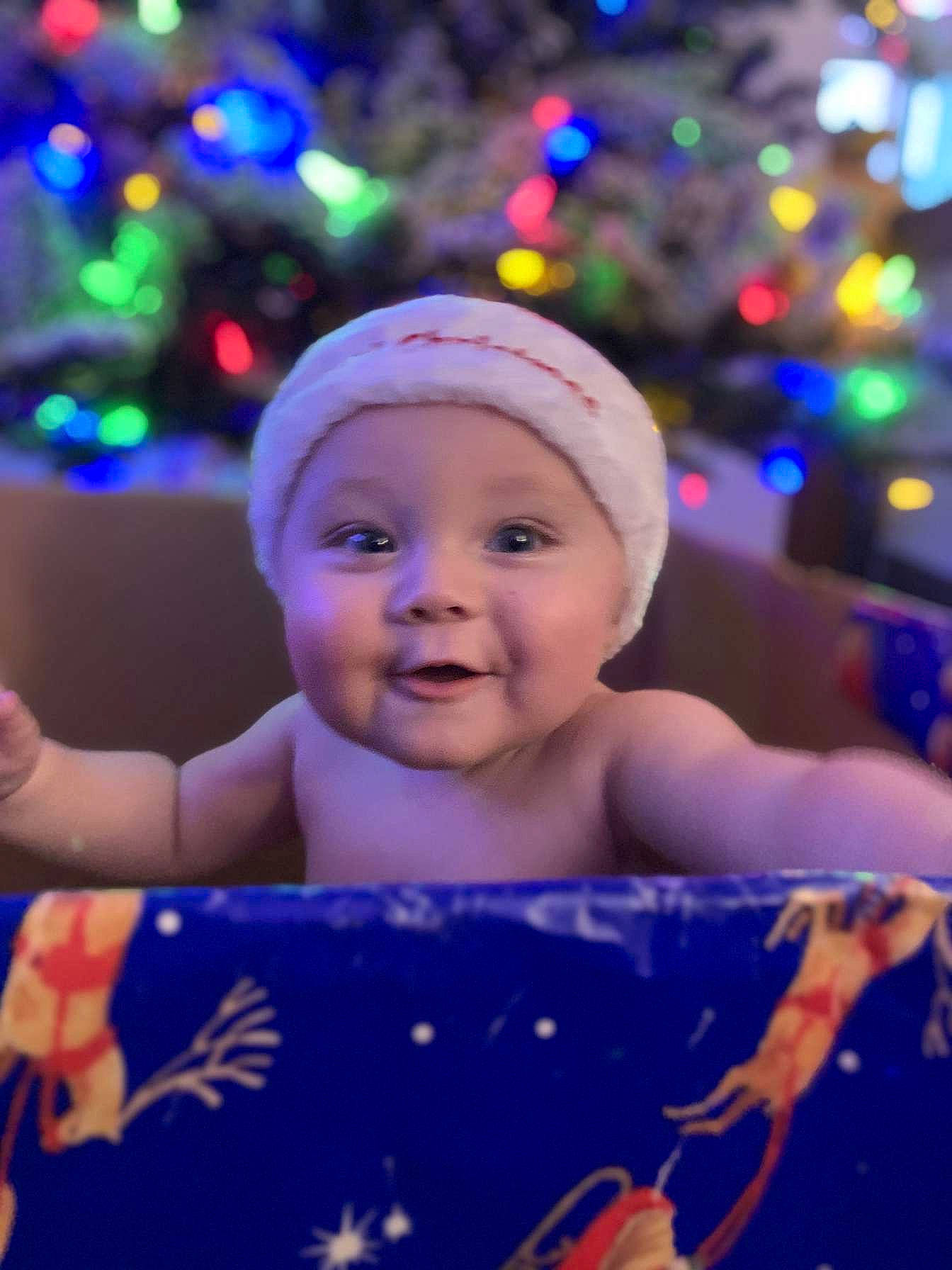 Devon is registered to the contest to win money with this photo: baby, child, christmas_decoration, christmas_ornament, christmas_tree, facial_expression, fun, happy, head, headwear, holiday, human_body, light, ornament, person, purple, sky, smile, standing, toddler